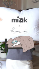 Людина тримає подушку з логотипами MINK × Home me та ілюстрацією кота під ковдрою.