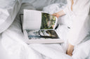 Читання відкритої книги в ліжку серед білої постільної білизни.